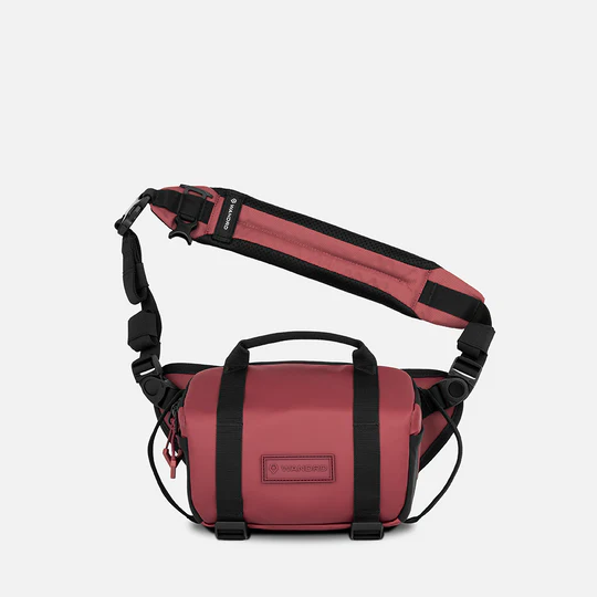 A burgandy and black crossbody bag with a top handle, front zippered pocket, and adjustable shoulder strap, shown against a light gray background.