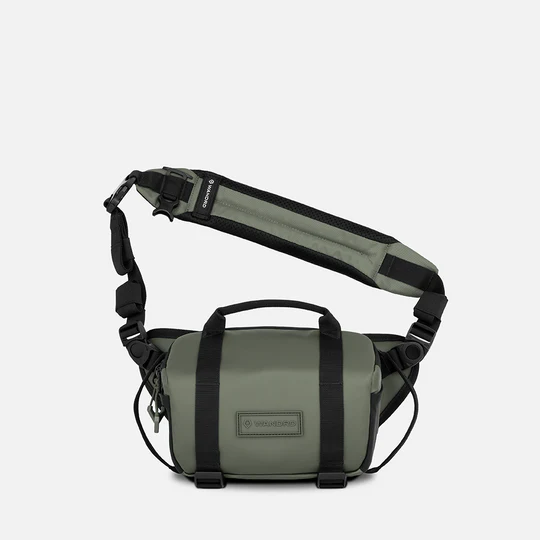 An olive green and black Wavers crossbody bag with an adjustable shoulder strap, top handle, and front zippered pocket, shown against a light gray background.