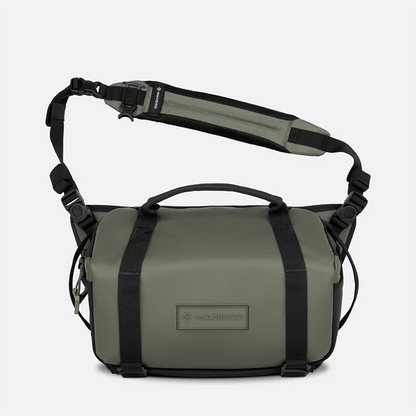 An olive green bag with black straps and a padded shoulder strap, featuring a top handle and a visible brand patch on the front.
